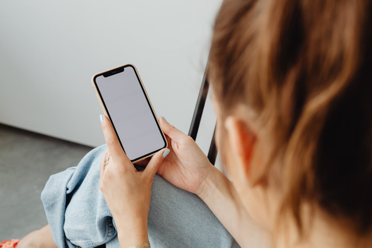 A woman holds a smartphone with a blank screen indoors, offering a mockup opportunity.